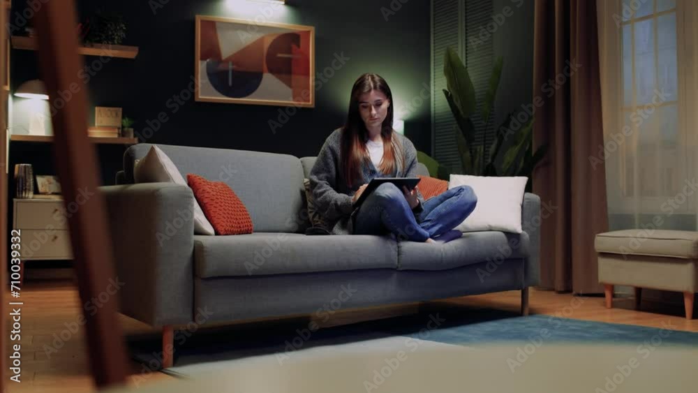 Woman relaxing sitting at sofa. Female sitting at couch with legs. Woman holding tablet and working. Female using device for working distantly. Woman freelancing at home. Woman relaxing sitting at sofa. Female sitting at couch with legs. Woman holding tablet and working. Female using device for working distantly. Woman freelancing at home.