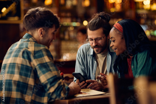 Young man and his friends using cell phone in bar.