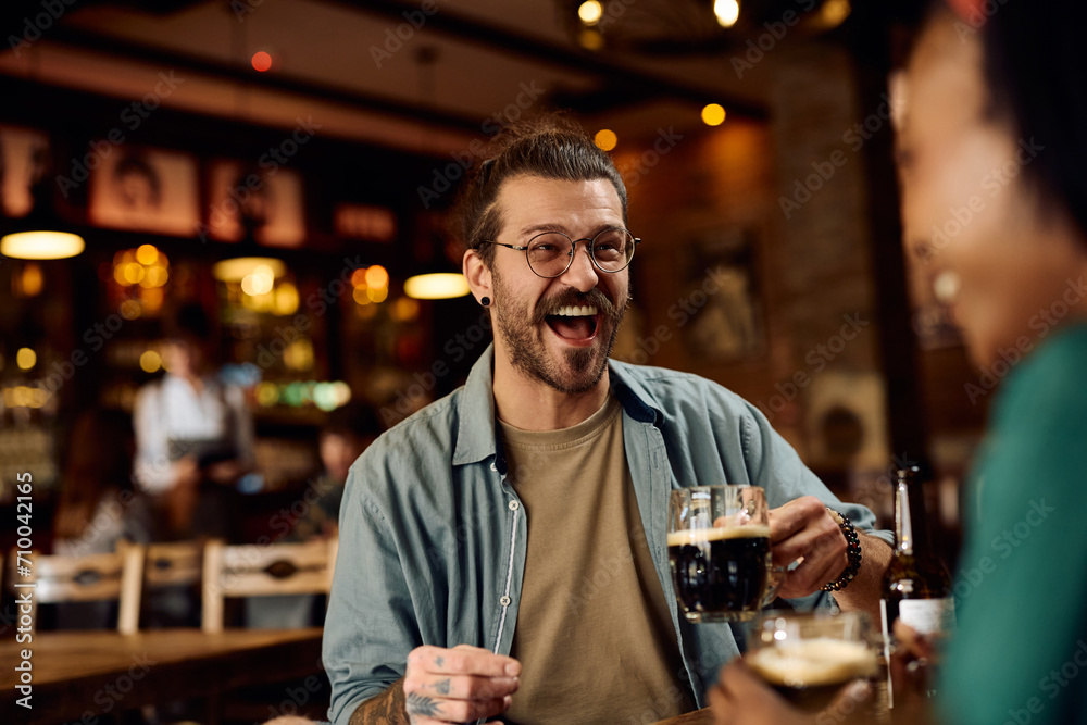 Young man laughing and having fun while drinking beer with girlfriend in pub.