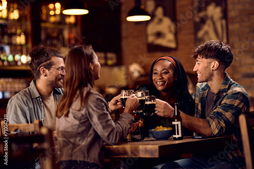 Multiracial group of happy friends toasting with beer while gathering in pub. © Drazen