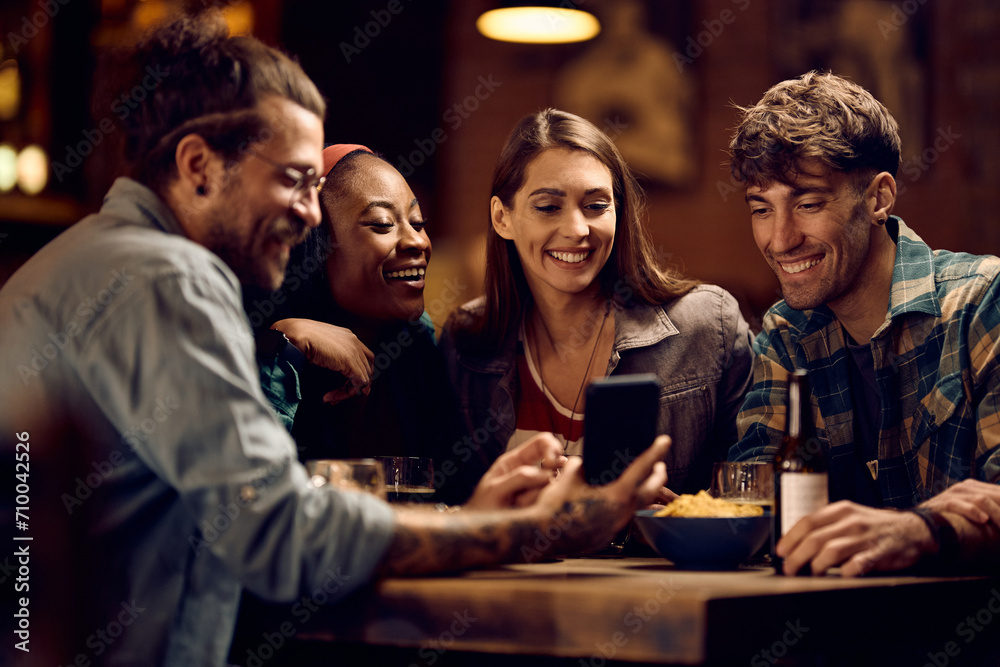 Group of happy friends using smart phone in pub. - obrazy, fototapety, plakaty 