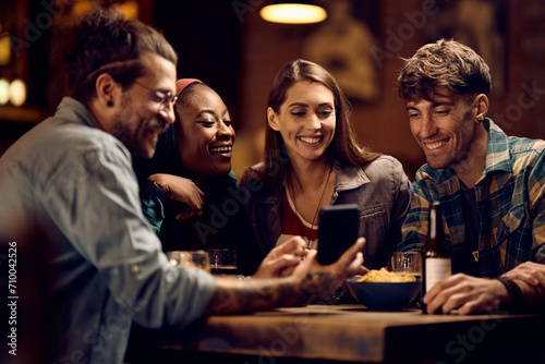 Group of happy friends using smart phone in pub.