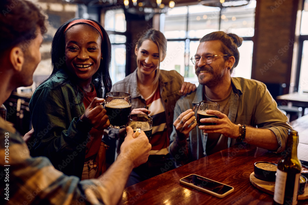 Happy black woman and her friends toasting with beer in bar.