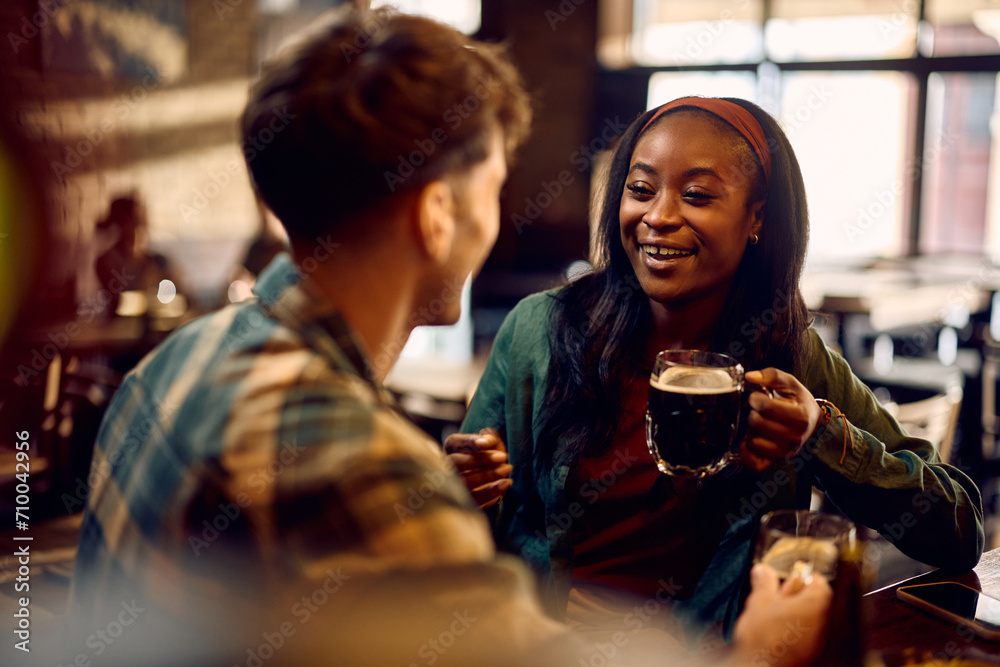 Happy black woman communicating with her friend while enjoying in glass of beer in pub.