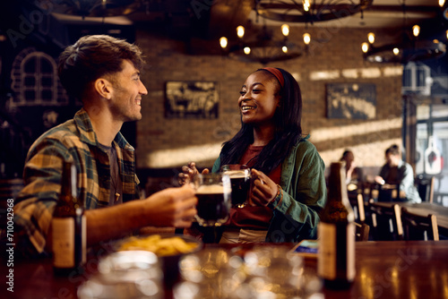 Happy black woman and her boyfriend talk while drinking beer in bar.