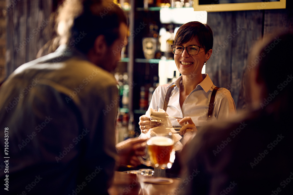 Happy waitress communicating with customers while cleaning glasses at bar counter.