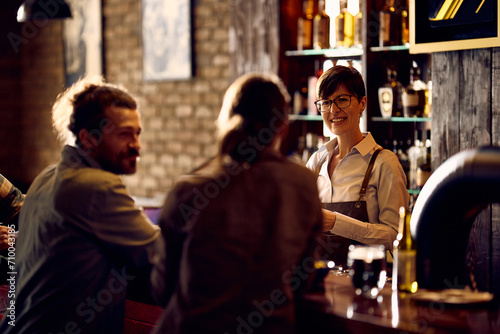 Happy waitress talking to couple while working at bar counter.