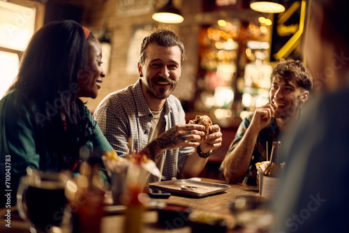 Happy man and his friends talk while enjoying in food and drinks in pub.