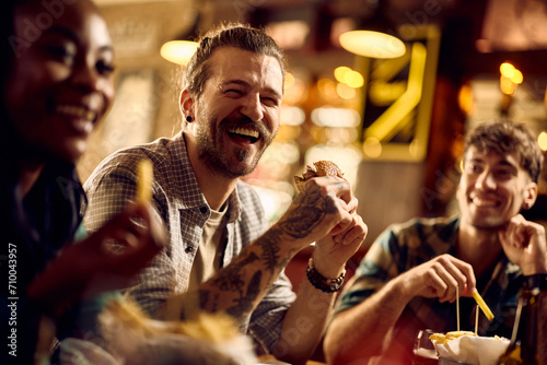 Fotografie Young man laughing and having fun while eating with his friends in pub