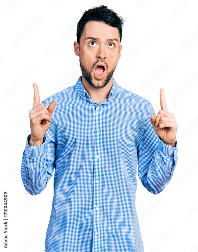 Hispanic man with beard wearing casual business shirt amazed and surprised looking up and pointing with fingers and raised arms. Hispanic man with beard wearing casual business shirt amazed and surprised looking up and pointing with fingers and raised arms.