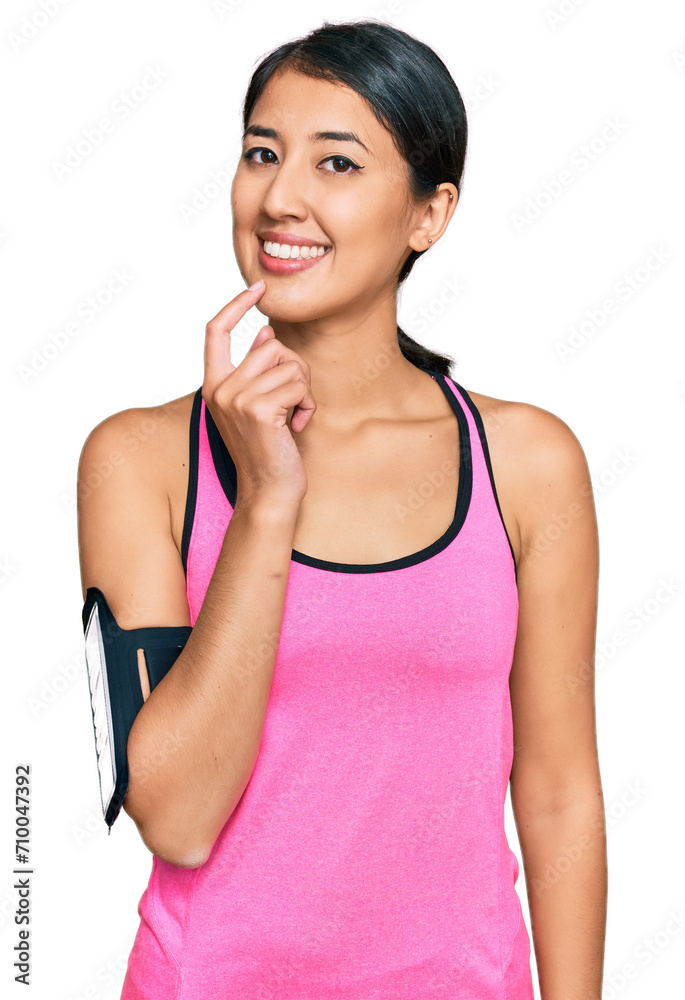 Beautiful asian young sport woman wearing sportswear and arm band looking confident at the camera with smile with crossed arms and hand raised on chin. thinking positive.