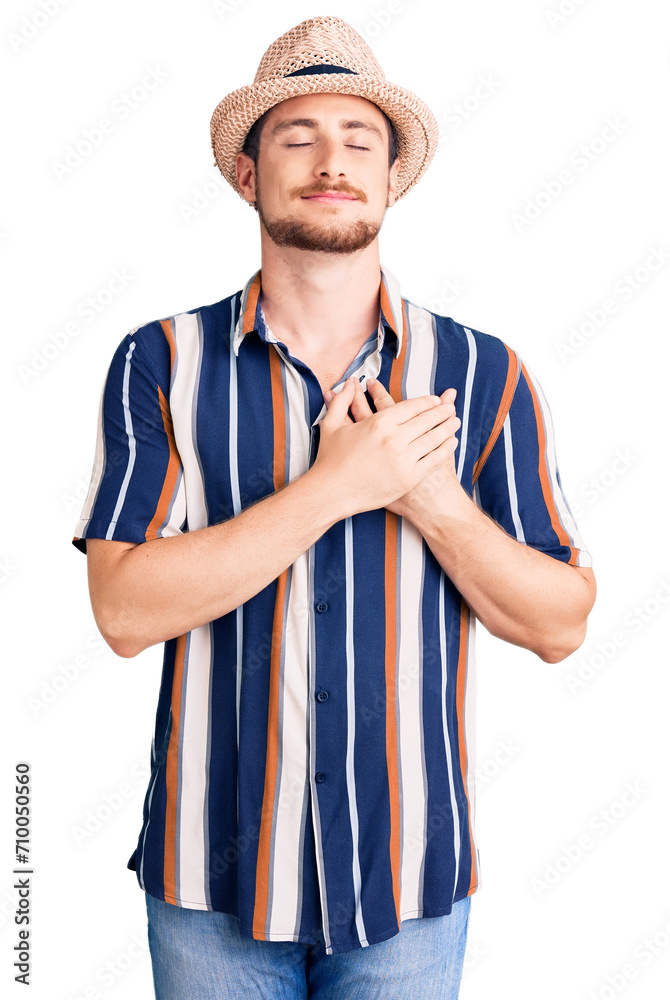 Young handsome caucasian man wearing summer hat smiling with hands on chest with closed eyes and grateful gesture on face. health concept. Young handsome caucasian man wearing summer hat smiling with hands on chest with closed eyes and grateful gesture on face. health concept.