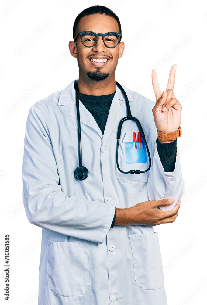 Young african american man wearing doctor uniform and stethoscope smiling with happy face winking at the camera doing victory sign with fingers. number two. Young african american man wearing doctor uniform and stethoscope smiling with happy face winking at the camera doing victory sign with fingers. number two.
