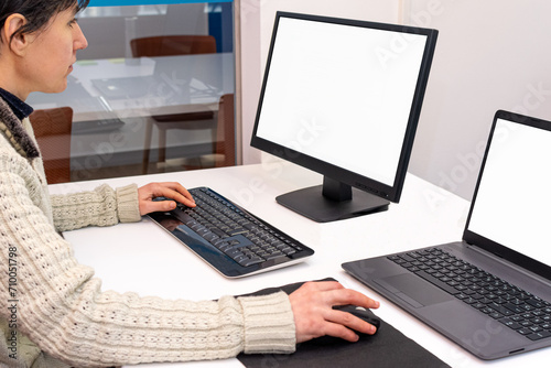 A woman working in the office driving a desktop computer and a laptop. Copy space on screen