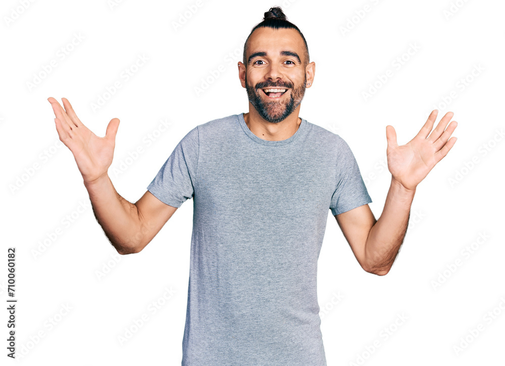 Naklejka premium Hispanic man with ponytail wearing casual grey t shirt celebrating crazy and amazed for success with arms raised and open eyes screaming excited. winner concept