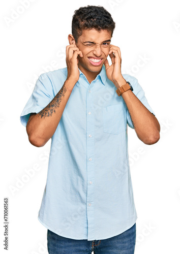 Young handsome african american man wearing casual clothes covering ears with fingers with annoyed expression for the noise of loud music. deaf concept. © Krakenimages.com