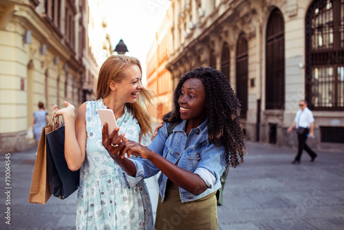 Diverse young women using smartphone and shopping in city