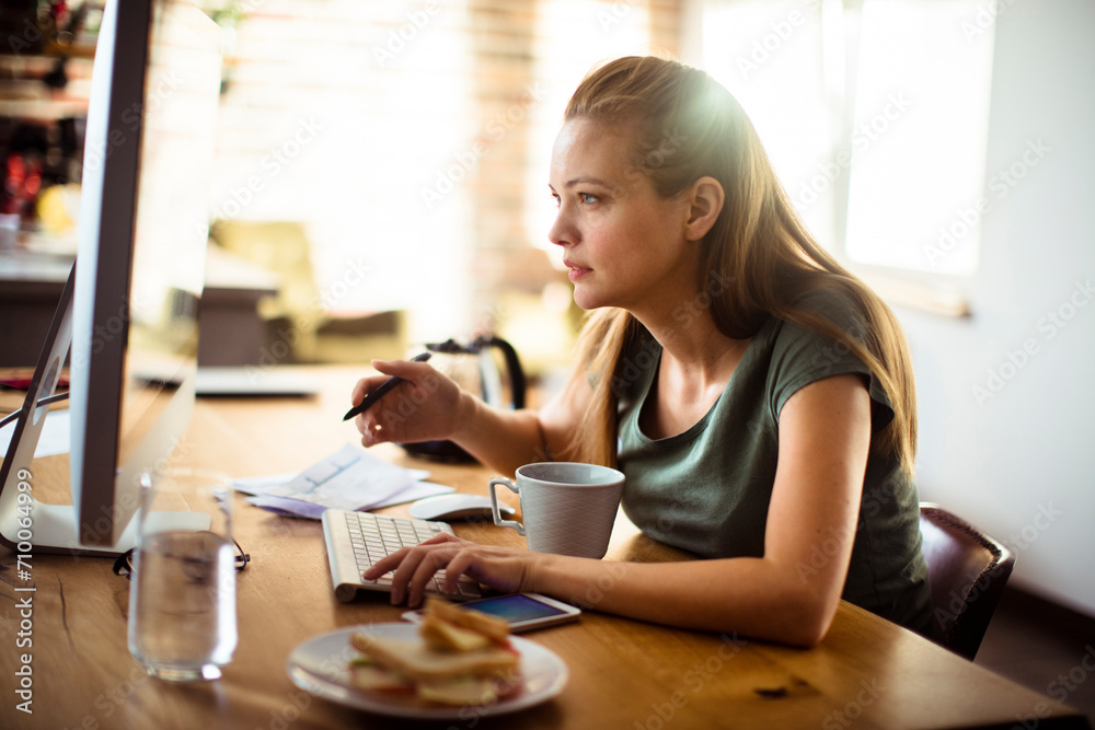 Freelancer working on computer with breakfast sandwich on desk Freelancer working on computer with breakfast sandwich on desk