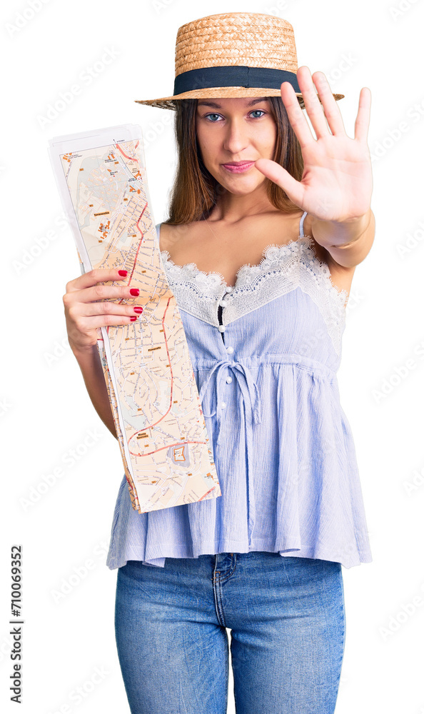 Beautiful brunette young woman wearing summer hat holding city map with open hand doing stop sign with serious and confident expression, defense gesture Beautiful brunette young woman wearing summer hat holding city map with open hand doing stop sign with serious and confident expression, defense gesture