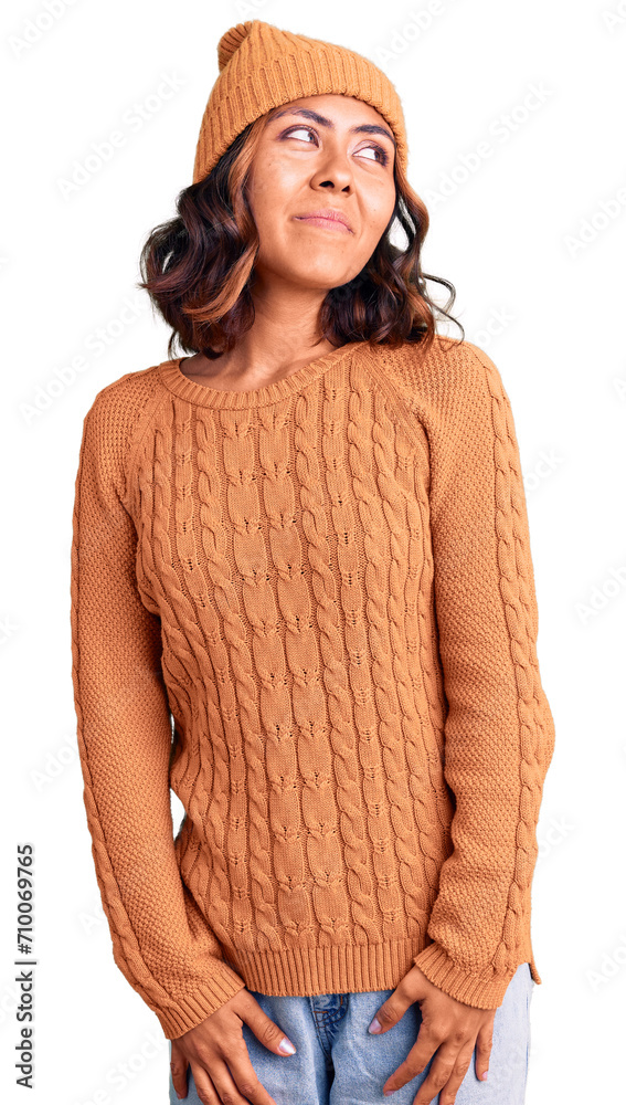 Young beautiful mixed race woman wearing wool sweater and winter hat smiling looking to the side and staring away thinking. Young beautiful mixed race woman wearing wool sweater and winter hat smiling looking to the side and staring away thinking.