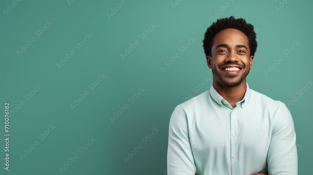 Fototapeta premium A cheerful young man wearing a mint green shirt radiates happiness against a matching turquoise background, perfectly illustrating a casual yet professional demeanor.