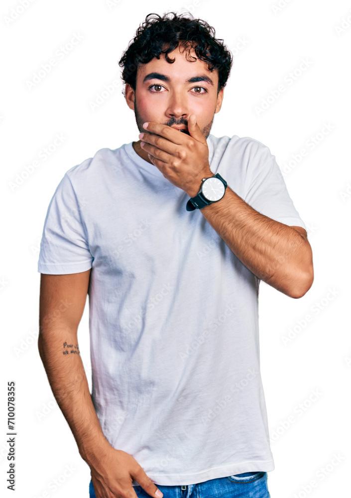 Hispanic young man with beard wearing casual white t shirt looking fascinated with disbelief, surprise and amazed expression with hands on chin Hispanic young man with beard wearing casual white t shirt looking fascinated with disbelief, surprise and amazed expression with hands on chin