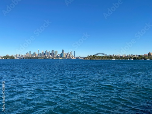 City skyline from the ocean shore. View of Sydney and its iconic buildings, skyscrapers and bridge at the distance. Australian city on the horizon. © Stephanie