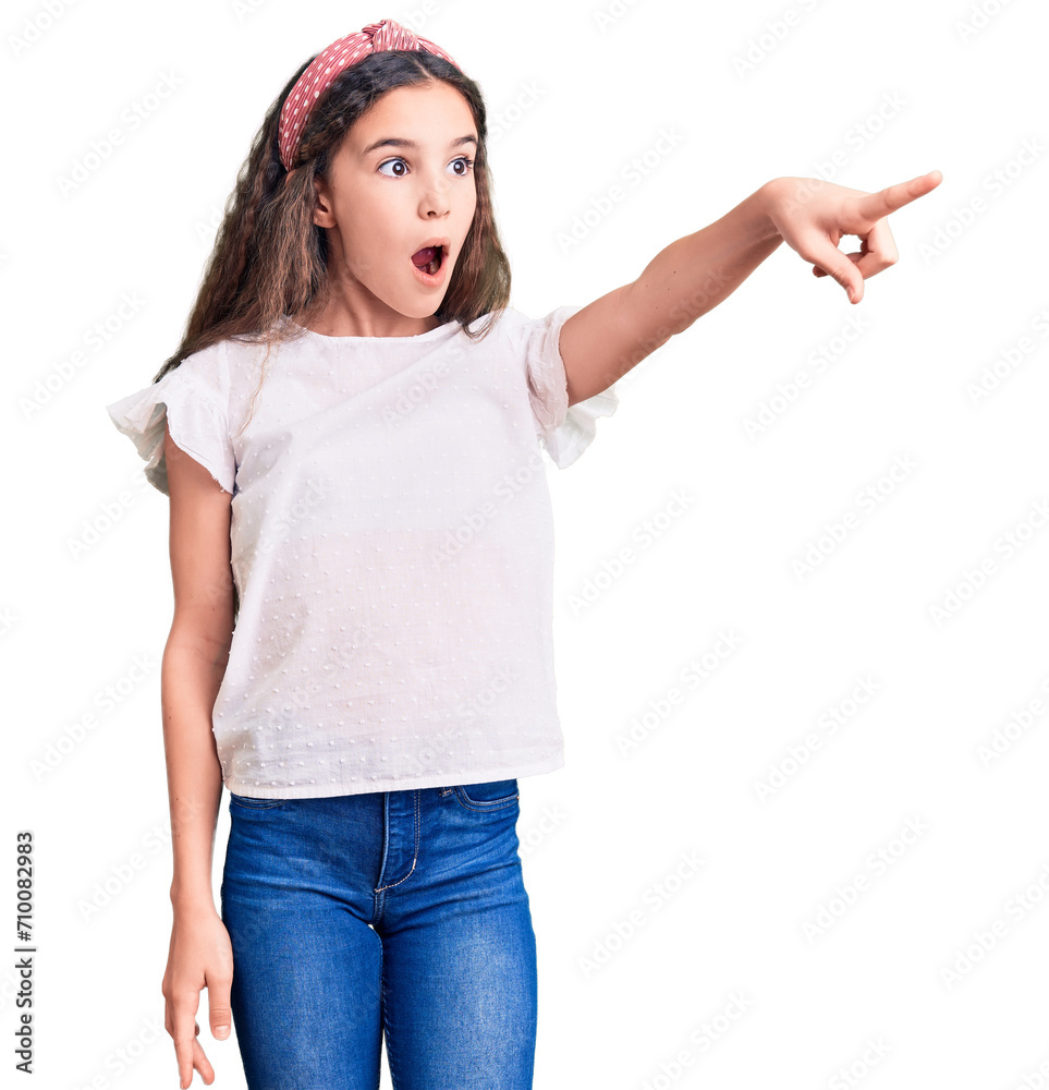 Cute hispanic child girl wearing casual white tshirt pointing with finger surprised ahead, open mouth amazed expression, something on the front Cute hispanic child girl wearing casual white tshirt pointing with finger surprised ahead, open mouth amazed expression, something on the front