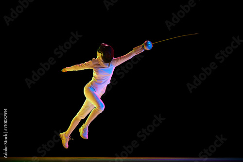 Sports training. Athlete demonstrating skill and form developed through dedicated sports training. Female fencer in motion over black background in neon. Concept of sport, competition, championship