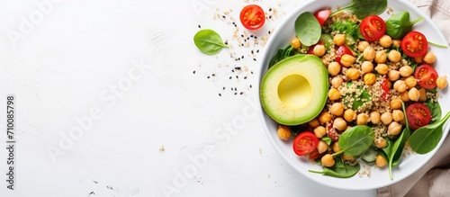 Top view vegetable salad with quinoa, avocado, tomato, spinach, and chickpeas - on white table.