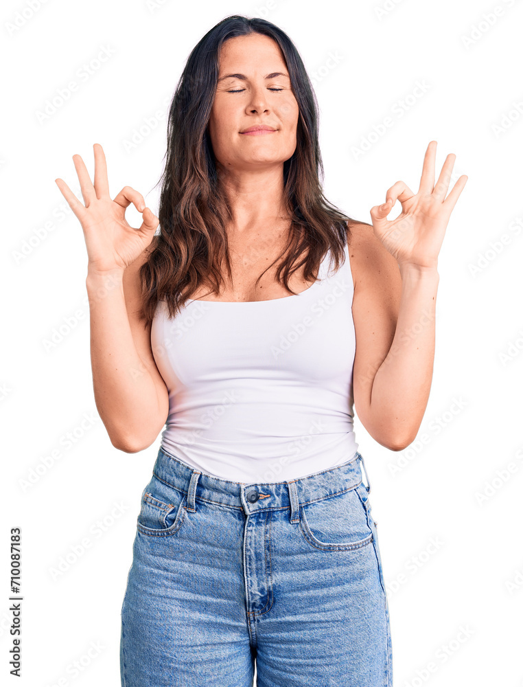 Young beautiful brunette woman wearing casual sleeveless t-shirt relax and smiling with eyes closed doing meditation gesture with fingers. yoga concept. Young beautiful brunette woman wearing casual sleeveless t-shirt relax and smiling with eyes closed doing meditation gesture with fingers. yoga concept.