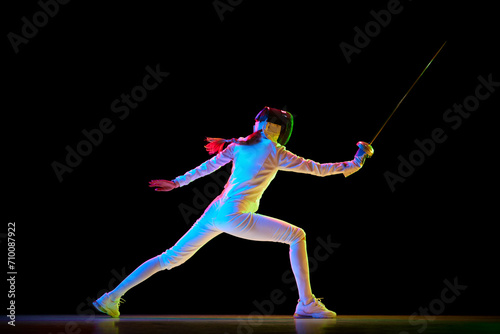 Self-defense skills. Although sportive, fencing skills can represent the broader theme of self-defense. Female athlete in motion, training over black background in neon. Concept of sport, competition