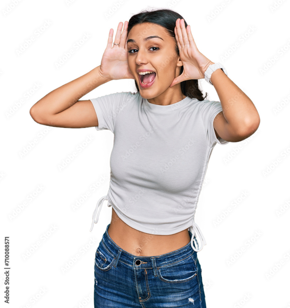 Young hispanic girl wearing casual white t shirt smiling cheerful playing peek a boo with hands showing face. surprised and exited Young hispanic girl wearing casual white t shirt smiling cheerful playing peek a boo with hands showing face. surprised and exited