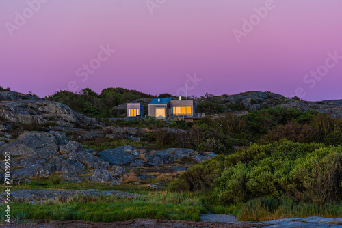 A small summer cottage by the coast in warm sunset light.