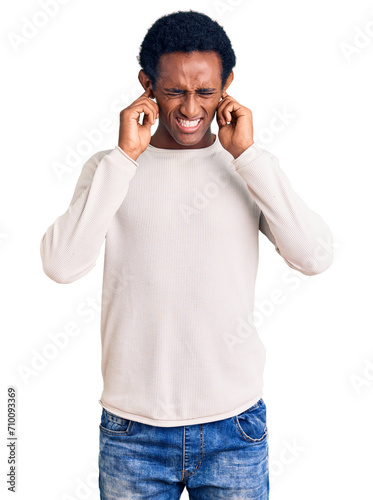 African handsome man wearing casual winter sweater covering ears with fingers with annoyed expression for the noise of loud music. deaf concept.