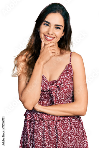 Beautiful hispanic woman wearing summer dress looking confident at the camera smiling with crossed arms and hand raised on chin. thinking positive.