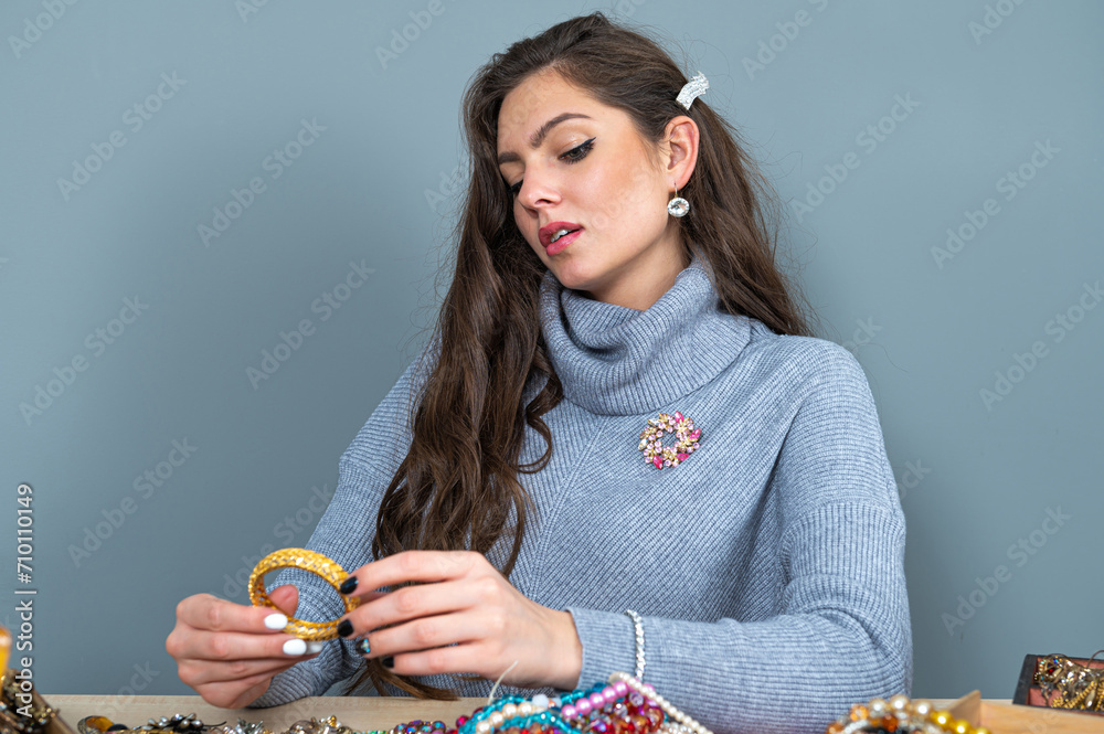 young brunette sitting at the table with lots of jewelry, choosing and trying different jewelry young brunette sitting at the table with lots of jewelry, choosing and trying different jewelry