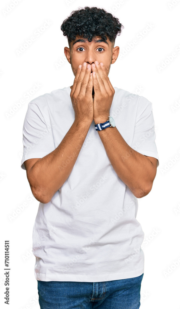 Young arab man wearing casual white t shirt laughing and embarrassed giggle covering mouth with hands, gossip and scandal concept Young arab man wearing casual white t shirt laughing and embarrassed giggle covering mouth with hands, gossip and scandal concept