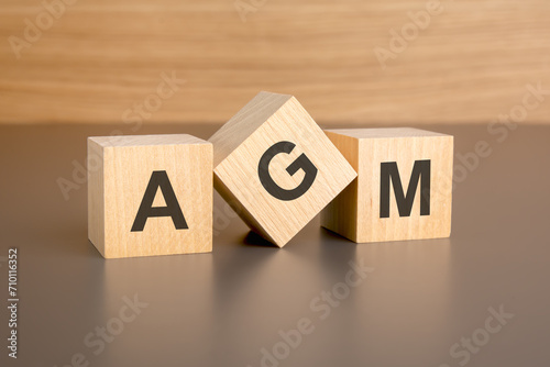 three wooden blocks on a brown background, with the abbreviation AGM - Annual General Meeting