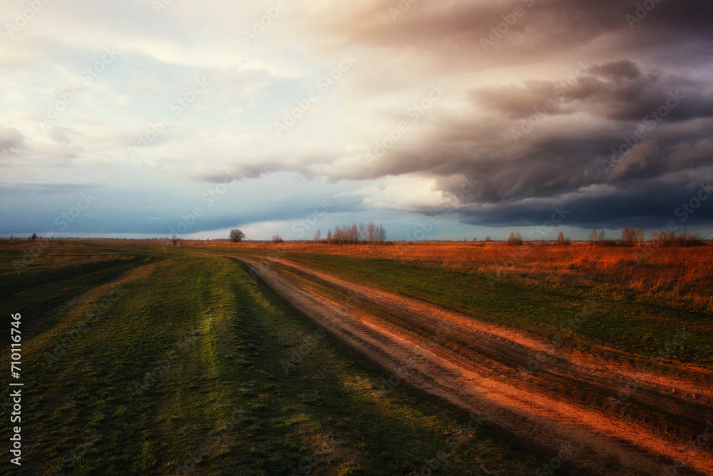 Clouds gather above a serene, open landscape with a long path.