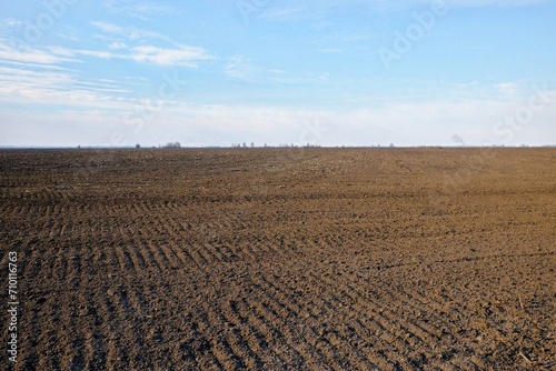 Фотография A vast field of plowed soil under a sky with scattered clouds.