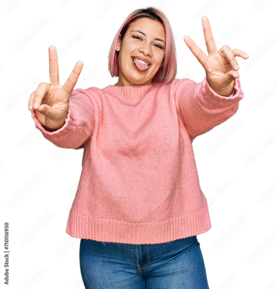 Hispanic woman with pink hair wearing casual winter sweater smiling with tongue out showing fingers of both hands doing victory sign. number two. Hispanic woman with pink hair wearing casual winter sweater smiling with tongue out showing fingers of both hands doing victory sign. number two.