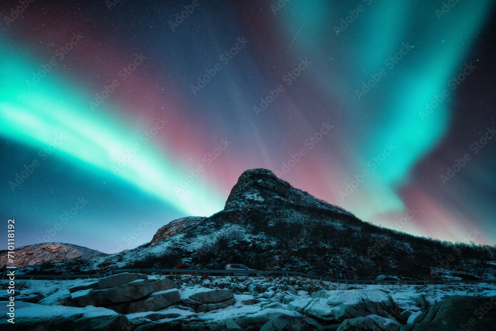 Northern lights and snowy mountains at night in Lofoten, Norway. Aurora borealis above the snow covered rocks. Winter landscape with polar lights, mountain peak. Starry sky with bright aurora