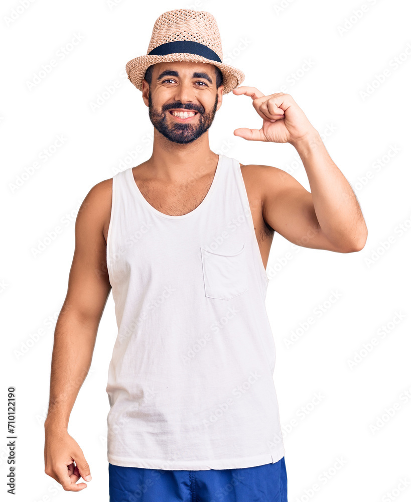 Young hispanic man wearing casual summer hat smiling and confident gesturing with hand doing small size sign with fingers looking and the camera. measure concept. Young hispanic man wearing casual summer hat smiling and confident gesturing with hand doing small size sign with fingers looking and the camera. measure concept.