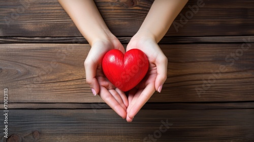 Close-up of a woman s hands holding a red heart on a wooden background. Valentine s Day greeting card. A symbol of love. View from above.