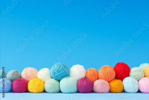Vibrant display of colorful wool yarn balls on solid sky blue background with ample space for text photo