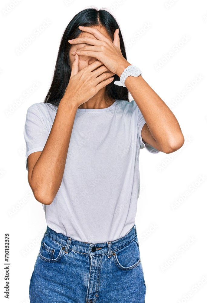 Beautiful young asian woman wearing casual white t shirt covering eyes and mouth with hands, surprised and shocked. hiding emotion Beautiful young asian woman wearing casual white t shirt covering eyes and mouth with hands, surprised and shocked. hiding emotion
