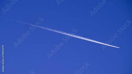 flying airplane in the cobalt blue sky, white plane trail on blue background