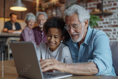 An elderly couple at home looking at a laptop with a multi-generational family in the background