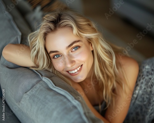 Smiling pretty blonde young woman wearing casual clothes lean on gray fabric sofa at home, close up.